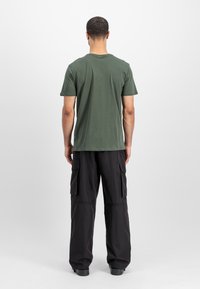 Grünes Baumwoll-T-Shirt mit kurzen Ärmeln und Rundhalsausschnitt, kombiniert mit lockeren schwarzen Cargo-Hosen mit zwei seitlichen Taschen.