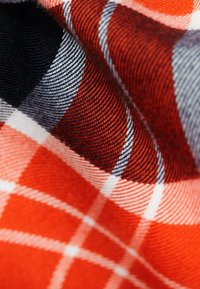 Tela de cuadros en rojo y negro con una textura tejida, con acentos en blanco y azul marino. El patrón incluye diseños de cuadros grandes y pequeños.