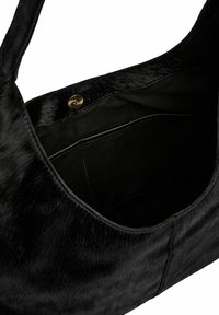 Čierna kožušinová kabelka s hladkou textúrou, zaobleným tvarom a zlatým zapínaním na cvok. Interiér obsahuje čiernu látku s detailom vrecka.