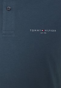Mörkblå polo t-shirt i mjukt tyg, med placket för två knappar och broderad "TOMMY HILFIGER EST. 1985" logga i vitt.