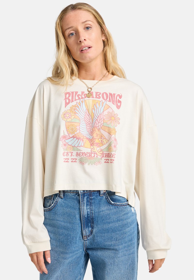 Cream-colored cropped long-sleeve t-shirt featuring a colorful graphic print of a bird and flowers. Paired with high-waisted blue jeans.