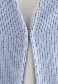 Vaaleansininen ribbineuleinen neuletakki, jossa on V-pääntie ja pehmeä rakenne. Siinä on hienovarainen kiilto ja siisti auki jäävä etuosa.