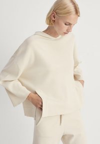 Jasnobeżowa bluza z kapturem o szerokich rękawach i bocznymi kieszeniami, wykonana z miękkiego materiału. Charakteryzuje się luźnym krojem i minimalistycznym wzornictwem.