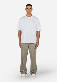 White cotton t-shirt with round neckline and short sleeves, featuring a black logo on the left side. Paired with light gray wide-leg pants.