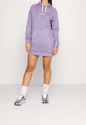 Person trägt ein lavendelfarbenes Hoodie-Kleid mit langen Ärmeln und Fronttasche, kombiniert mit weißen Socken und blau-weißen Laufschuhen.