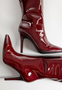 Talons en cuir verni bourgogne et bottes jusqu'au genou avec un fini brillant, présentant des talons aiguilles fins et des silhouettes ajustées et élégantes.