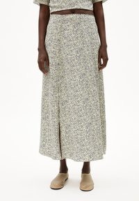 Maxi-jurk van een lichtgroene stof met een verspreide marineblauwe print, heeft een voorkant-split en een elastische tailleband. Gecombineerd met beige instapschoenen.