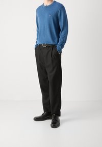 Niebieski melanżowy sweter dziany o luźnym kroju; czarne plisowane spodnie; czarne buty z zaokrąglonymi czubkami. Proste okrągłe zapięcie paska.