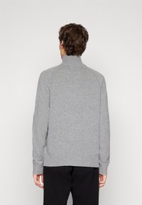 Pull en gris, texturé, avec un col haut et des poignets côtelés. Il présente une coupe décontractée, des manches longues et est confectionné en un tissu tricoté doux.