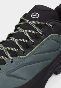 Κοντινή όψη ενός μαύρου και γκρι παπουτσιού πεζοπορίας με κορδόνια με σχέδιο και στρογγυλό λογότυπο στη γεμισμένη γλώσσα.