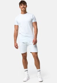 Tricou din bumbac de culoare bleu deschis, asociat cu pantaloni scurți asortați. Materialul este neted, cu mâneci scurte și gât rotund. Pantofi atletici albi.