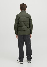 Vadderad olivgrön jacka med hög krage, kombinerad med mörkgrå vida jeans och svartvita sneakers. Enkel design, inga mönster.