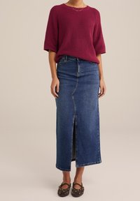 Burgundská pletená svetřík s krátkými rukávy, spárovaný s tmavě modrou maxi sukní z denimu s předním rozparkem a tmavě hnědými botami se hroty.