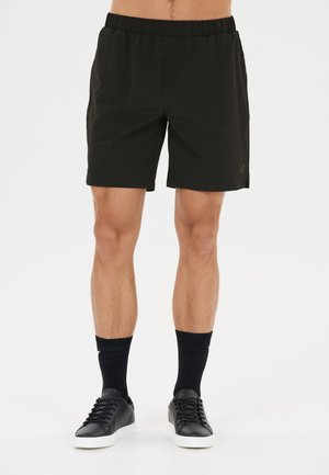 Man wearing black elastic waist shorts, black mid-calf socks, and black sneakers with white soles, standing against a white background.