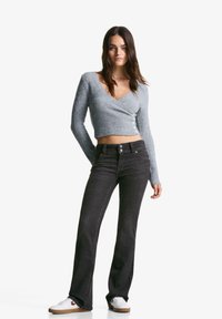 Light gray cropped sweater with ribbed texture and button detail, paired with dark flared jeans and white sneakers.