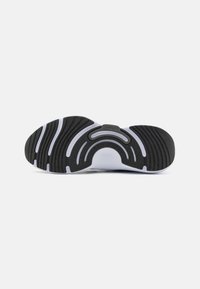 Zwart rubberen zool van een sneaker met witte gebogen groeven en een gestructureerd patroon. Heeft een centrale uitsparing en een klein logo in grijs.