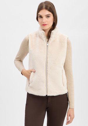 Nepluizige foute vest in crèmekleur met een hoge kraag, ritssluiting aan de voorkant en zijzakken, gecombineerd met een beige top met lange mouwen en een paarse broek.