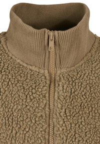 Rjavi flis pulover z zadrgo, visokim rebrastim ovratnikom in teksturirano tkanino. Ima osrednjo zadrgo v usklajeni rjavi barvi.