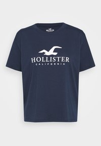 Camiseta de algodón azul marino con un logo de gaviota blanca y el texto "HOLLISTER CALIFORNIA" en el pecho, con mangas cortas y cuello redondo.