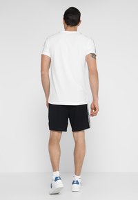 Vit kortärmad t-shirt med rund halsringning, matchad med svarta shorts med sidosträck, avslutad med vita sneakers.