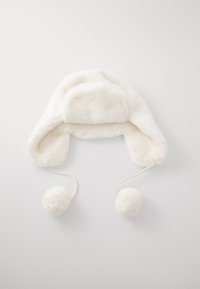 Chapeau en fourrure synthétique blanche avec rabats d'oreilles, sommet arrondi, et deux pompons aux extrémités des liens. Texture lisse, aspect doux, et sans coutures visibles.