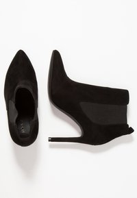 Černé semišové kotníkové boty na vysokém podpatku s špičatou špičkou, elastickým bočním panelem a metalickým akcentem na podpatku. Hladký povrch, moderní design.