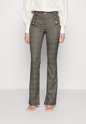 Szare w kratę spodnie z wysokim stanem, z guzikami przy biodrach, noszone z białą bluzką i beżowymi sandałami na odkryte palce.