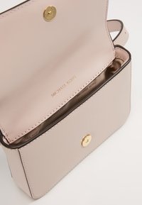 Světlé růžové kožené crossbody taška se zlatými kovovými detaily, uzavírání na patenty a vnitřní podšívka z béžové látky s embosovaným logem.
