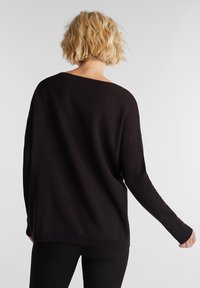 Svart oversize tröja med lös passform, vid halsringning och långa ärmar. Mjuk textur med ribbad nederkant och ärmslut, minimalistisk design.