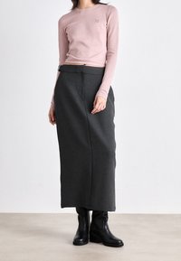 Jasnoróżowa dopasowana bluzka z długim rękawem i okrągłym dekoltem. Ciemnoszara spódnica ołówkowa z wysokim stanem i gładką fakturą, zestawiona z czarnymi botkami za kostkę.