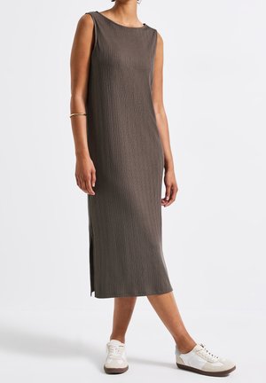 Mouwloze, ribbel midi-jurk in olijfgroen met zijslits. Combinatie met witte en beige sneakers. Eenvoudige, rechte silhouet.