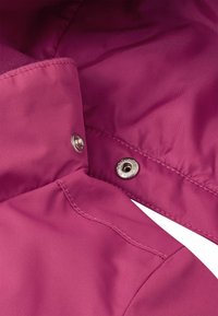 Růžová textilie s hladkým povrchem, s límcem a stříbrnými zarážkami. Tkanina vykazuje mírný lesk a čisté švy.