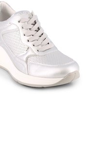 Zapatilla metálica plateada con diseño perforado, cordones planos y suela blanca elevada. Textura suave con punta redondeada y acentos mínimos.