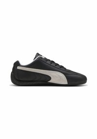 Baskets noires à profil bas avec bande blanche du logo sur le côté, lacets noirs et semelle fine noire, vues de profil gauche.