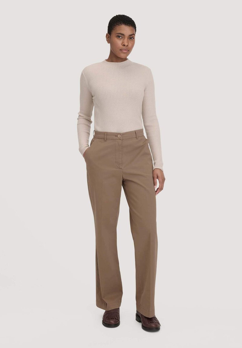 Beige geribbelde lange mouwen top gecombineerd met tan rechte pijpen broek met zijzakken en een riemlus, gecombineerd met bruine schoenen.