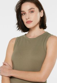 Olivgrünes, geripptes Tanktop mit rundem Ausschnitt und ärmellosem Design, das eine subtile Schulternaht und eine glatte Textur aufweist.