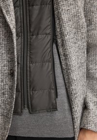 Gepolsterte graue Jacke mit einer strukturierten Außenschicht, schwarzen Reißverschlüssen und einem gemütlichen Strickfutter. Verfügt über eine Knopfverschluss und ein geschichtetes Design.