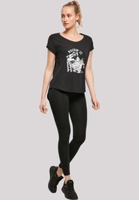 Svart t-skjorte med korte ermer og rund hals, med et hvitt grafisk trykk som står "ROCKIN' IT!" Kombinert med svarte leggings og sneakers.