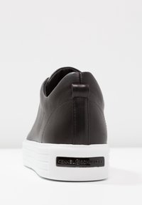 Sneaker nera in pelle con superficie testurizzata, forma arrotondata, suola bianca e linguetta sul tallone. Presenta una piastra con logo sul tallone.