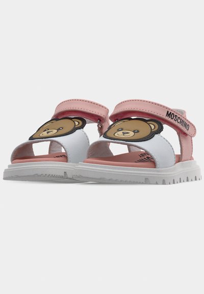 Ανοιχτά σανδάλια παιδικά με ροζ λουράκια, λευκές σόλες και διακοσμητικά με πρόσωπο αρκούδας, με την ένδειξη Moschino στα λουράκια αστραγάλου.