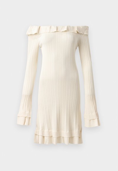 Krema haljina bez naramenica izrađena od rebraste tkanine, sa volanima na izrezu i manžetama rukava, koja ima prilagođen siluetu.