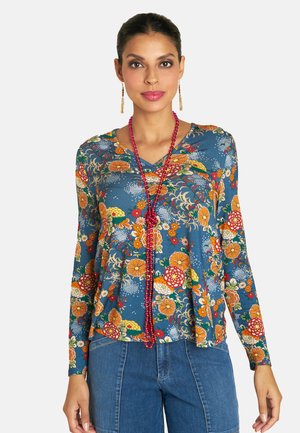 Floral long-sleeve top in blue fabric featuring vibrant orange, yellow, and green patterns. Paired with denim bottoms and a beaded necklace.