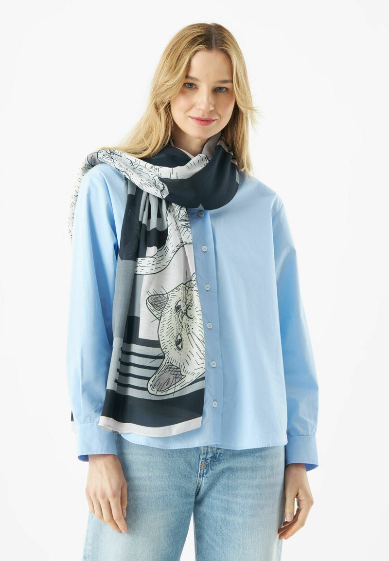 Zijden sjaal met een zwart-wit tekening van een dier op een lichte achtergrond, om de nek van een model gedrapeerd, gecombineerd met een blauwe blouse.