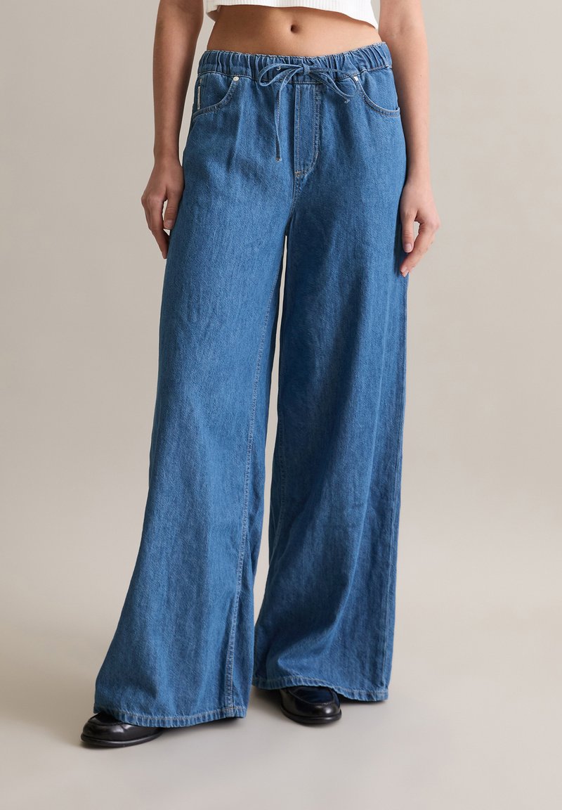 Jean large bleu clair en denim, avec une taille élastique à cordon de serrage et des poches avant. Ourlet à finition plate.