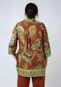Brown tunic with turquoise paisley and floral patterns, three-quarter sleeves, and a green hem. Smooth fabric and loose fit.