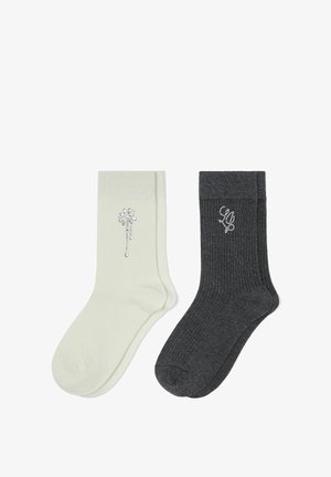 Un par de calcetines crema con un pequeño diseño floral de pedrería y un par de calcetines acanalados gris oscuro con un monograma de pedrería.