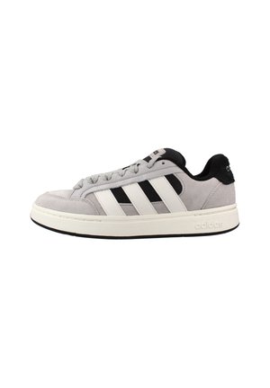 Zapatilla baja gris de Adidas con rayas blancas, detalles en negro, cierre de cordones y suela blanca sobre fondo blanco.