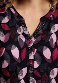 Blouse en tissu noir avec des motifs de feuilles roses et bordeaux. Présente un col en V avec des boutons décoratifs et des accents métalliques le long de la patte de boutonnage.