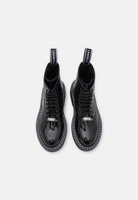 Black patent leather ankle boots with lace-up front, white stitching, and a branded pull tab. Features a smooth, glossy texture.
