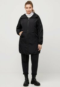 Svart vindjacka med dragkedja fram, huva, elastiska ärmslut och sidofickor. Tillverkad av ett tunt, lätt material.